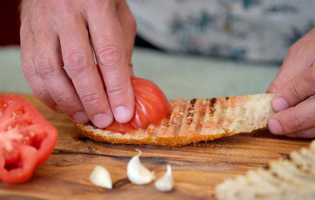 3. Tomaten gnis så mot brødet. Skvis tomaten lett mellm fingrene slik at kjerner fester seg på brødet.