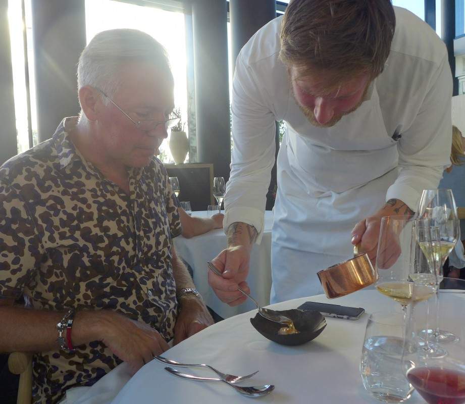 Esben Holmboe Bang serverer selv ved bordet. Her øses husets egen kombucha over rå kamskjell med rips og rogn. Høyrøkt skorsonerrotkrem under.